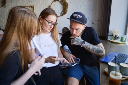 Três jovens conversam e usam dispositivos eletrônicos juntos em um café.