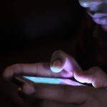 Pessoa segura e usa um smartphone iluminado em um ambiente escuro.