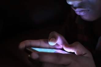 Pessoa segura e usa um smartphone iluminado em um ambiente escuro.