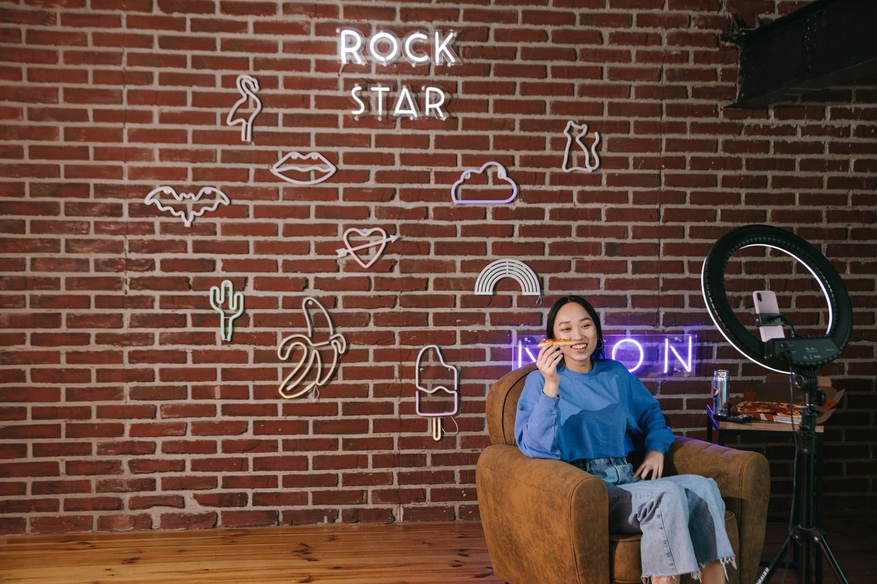 Criadora de conteúdo realiza uma transmissão ao vivo em um ambiente com iluminação neon e decoração moderna.